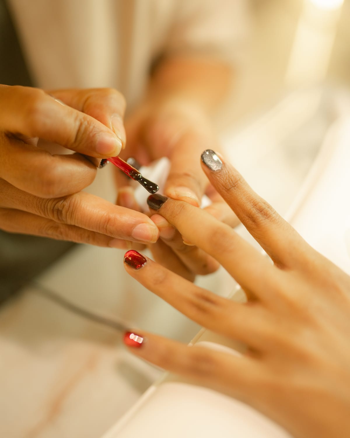 Technician painting a clients nails with dark red gel polish at the lounge