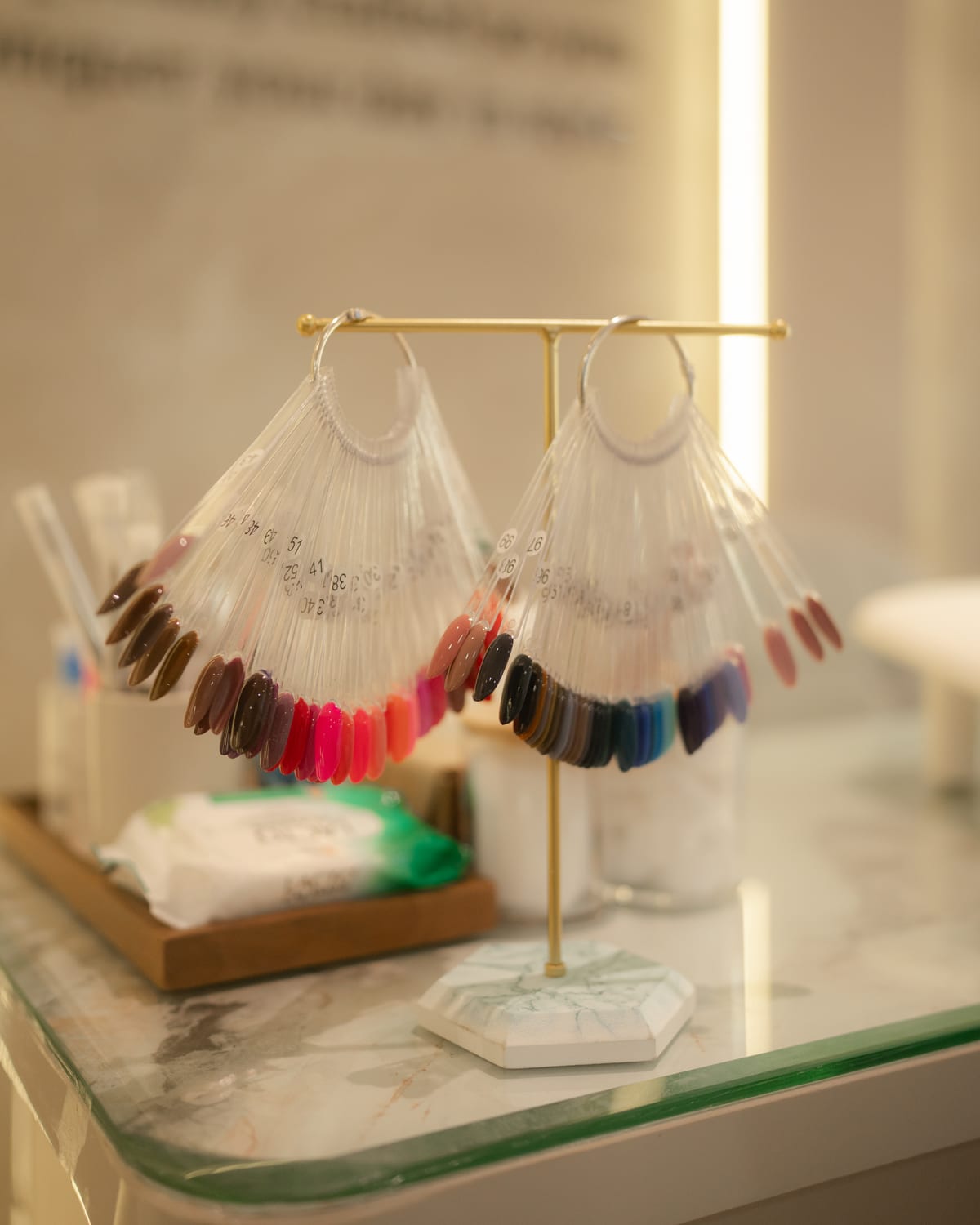 Two fanned nail colour swatches in a brass stand on a marble counter